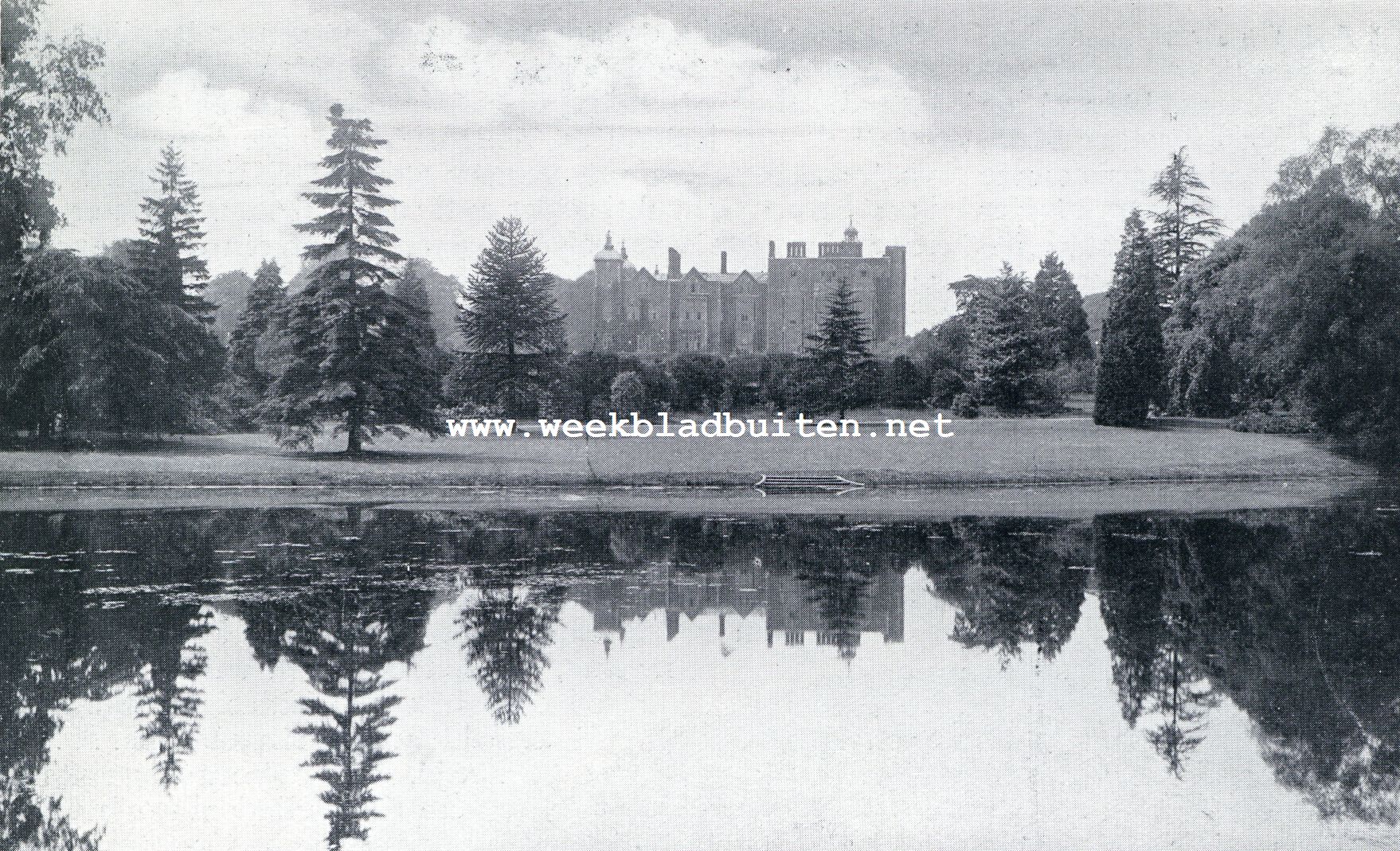 Hatfield House vanaf den vijver gezien, het blank van den bloei van statige kastanjes en lieflijke meidoorns is wazig.